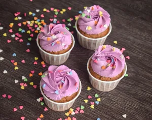 Delicious cupcakes topped with purple frosting and vibrant heart sprinkles on a wooden surface. jigsaw puzzle