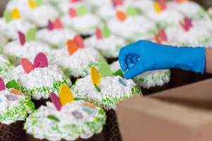 Crop unrecognizable worker in disposable glove with box against tasty desserts with egg and floral decor on whipped meringue cream jigsaw puzzle