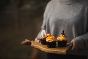 Three Halloween-themed cupcakes with spooky designs on a wooden tray being held. jigsaw puzzle