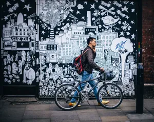 Man walking a bicycle past a detailed urban graffiti mural in a city setting. jigsaw puzzle