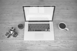 Monochrome image of a laptop, camera, lens, and coffee cup on a wooden desk jigsaw puzzle