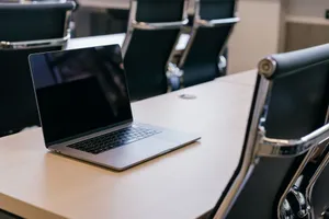 Open laptop on a wooden conference table with stylish black chairs in a modern office setting. jigsaw puzzle