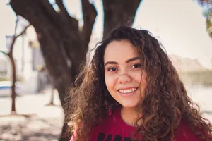 Portrait of a smiling young woman with curly hair in a sunny outdoor setting. jigsaw puzzle