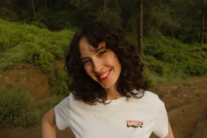 A cheerful woman with curly hair smiling outdoors in a green forest setting. jigsaw puzzle