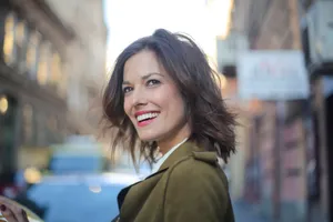 Portrait of a smiling woman standing on a city street in a green coat, looking away delightfully. jigsaw puzzle
