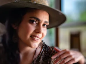Close-up portrait of a smiling woman in a hat, captured in natural light indoors. jigsaw puzzle