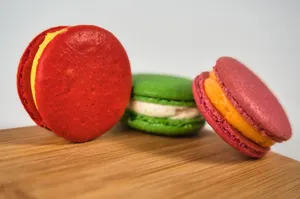 Colorful macaron trio on wood, showcasing red, green, and pink hues in a close-up shot. jigsaw puzzle