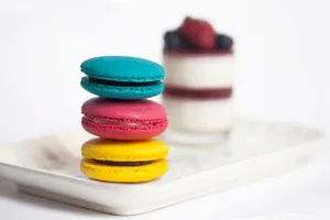 Brightly colored French macarons stacked on a plate with a berry-topped dessert in the background. jigsaw puzzle