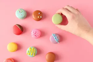 Vibrant French macarons on a pink background with a hand holding one. Perfect for dessert lovers. jigsaw puzzle