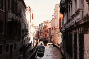 Explore a picturesque Venetian canal with boats and pedestrians strolling under the warm sun. jigsaw puzzle