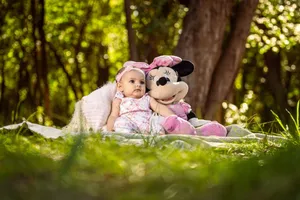 A cute baby sits outdoors with a Minnie Mouse toy, enjoying a sunny picnic day. jigsaw puzzle