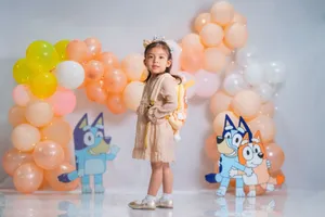Young girl at a birthday party surrounded by colorful balloon decorations and cartoon cutouts. jigsaw puzzle