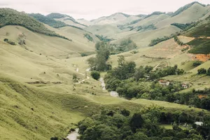 A breathtaking view of a lush green valley with rolling hills, trees, and a river. jigsaw puzzle