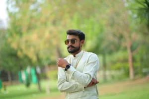 A confident South Asian man poses in traditional attire outdoors in a lush park setting. jigsaw puzzle