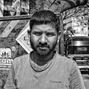 Black and white portrait of a bearded man standing outdoors in an urban setting. jigsaw puzzle