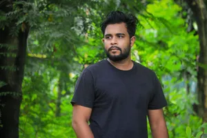 Close-up portrait of a bearded man in a black crew neck t-shirt, looking away in a lush green outdoor setting. jigsaw puzzle