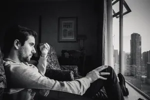 A thoughtful man with facial hair sits alone indoors, gazing at the city skyline. jigsaw puzzle