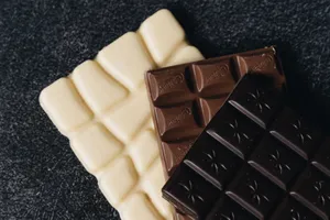 Close-up of assorted white, milk, and dark chocolate bars on a textured surface. jigsaw puzzle