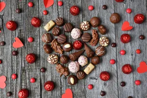Assorted chocolates arranged in a heart shape on weathered wooden planks with red accents, perfect for romantic themes. jigsaw puzzle
