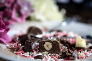Delightful close-up of assorted chocolate candies surrounded by colorful sprinkles and blurred floral background. jigsaw puzzle