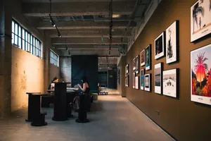 Art gallery hallway with framed artworks and visitors seated inside, under warm lighting. jigsaw puzzle