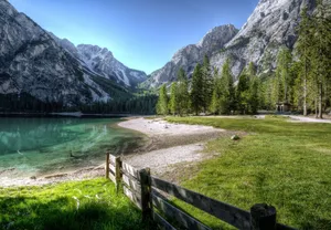 Serene mountain lake with green trees and a rustic fence, perfect nature backdrop. jigsaw puzzle