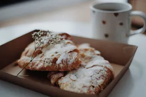 A pair of sugar-dusted croissants next to a coffee cup in a relaxed indoor setting. jigsaw puzzle