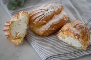 Tantalizing cream-filled pastries dusted with sugar on a striped cloth. Perfect dessert capture. jigsaw puzzle