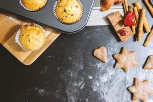 A delicious arrangement of muffins and cookies with cinnamon and flour on a black countertop. jigsaw puzzle