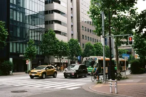 A bustling Tokyo street with cars, a bus, and a bicyclist on a warm day. jigsaw puzzle