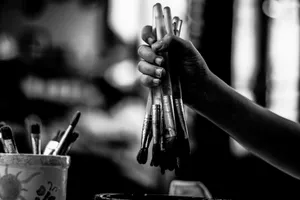 Hand holding a bunch of paintbrushes in a monochrome artistic setting. jigsaw puzzle