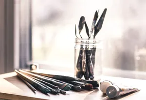 Glass jar with palette knives and paintbrushes on a sunny table, evoking creativity. jigsaw puzzle