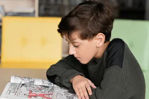 A young boy deeply focused on reading a comic book in a cozy indoor setting. jigsaw puzzle