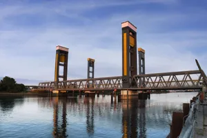 A modern drawbridge reflects over a calm river during daylight. jigsaw puzzle