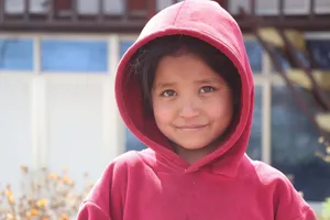 A young girl with a red hoodie smiling warmly while standing outdoors. jigsaw puzzle
