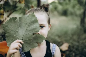 A charming young girl playfully holding a leaf in an outdoor setting, showcasing innocence. jigsaw puzzle