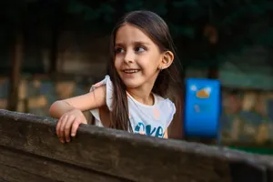 Young girl smiling while leaning on a wooden bench outdoors in a park setting. jigsaw puzzle