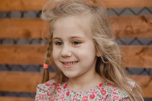 Candid portrait of a smiling girl with blonde hair and floral dress against a wooden background. jigsaw puzzle