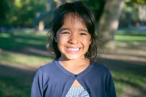A young girl smiling brightly outdoors in a sunlit park, capturing joyful childhood moments. jigsaw puzzle
