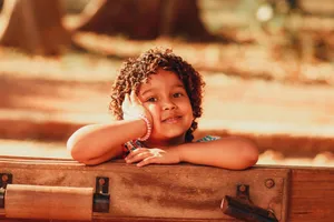 A cheerful young girl with curly hair resting on a bench in a sunny park. jigsaw puzzle
