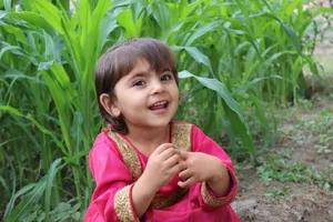 A young girl with a bright smile sitting amidst lush green plants, exuding joy and innocence. jigsaw puzzle