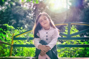 A young girl in stylish attire sitting on a bench in a sunny outdoor garden setting. jigsaw puzzle