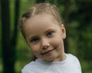 Close-up portrait of a smiling child in a lush forest. Soft focus with natural light and greenery. jigsaw puzzle