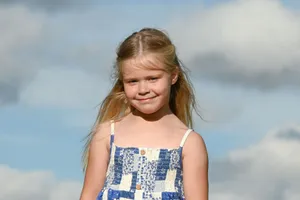 Happy child in a blue dress enjoying a sunny day outdoors with a bright sky in the background. jigsaw puzzle