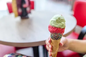 Hand holding a colorful ice cream cone topped with mint and raspberry scoops indoors. jigsaw puzzle