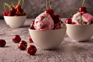 Three white ceramic bowls filled with cherry ice cream and fresh cherries on a textured surface. jigsaw puzzle