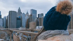 A woman in a winter hat looks at the city skyline from a bridge with clear blue skies. jigsaw puzzle