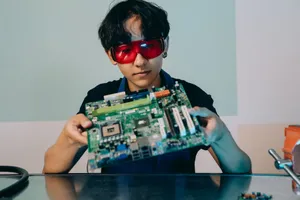 A focused young engineer holding a motherboard, wearing eye protection indoors. jigsaw puzzle