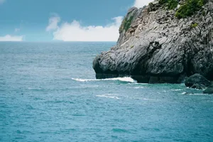 A striking rocky sea cliff with blue ocean waves and cloud-dappled sky. jigsaw puzzle