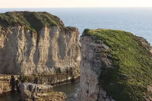 Scenic view of rocky cliffs with greenery against a tranquil sea backdrop. jigsaw puzzle